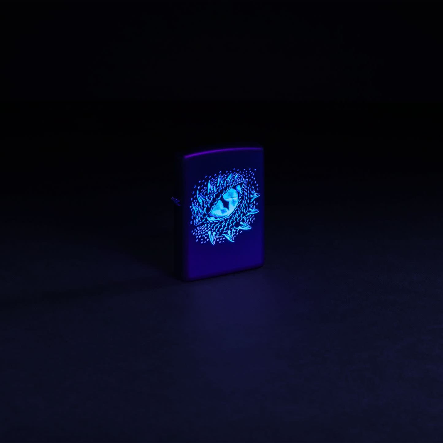 Glamour shot of Zippo Black Light Dragon Eye Design Black Matte Windproof Lighter glowing with a black light.