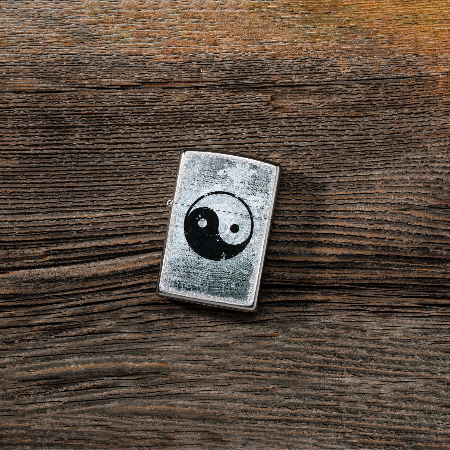 Lifestyle image of Yin Yang Design Street Chrome™ Windproof Lighter laying on a wooden table. 