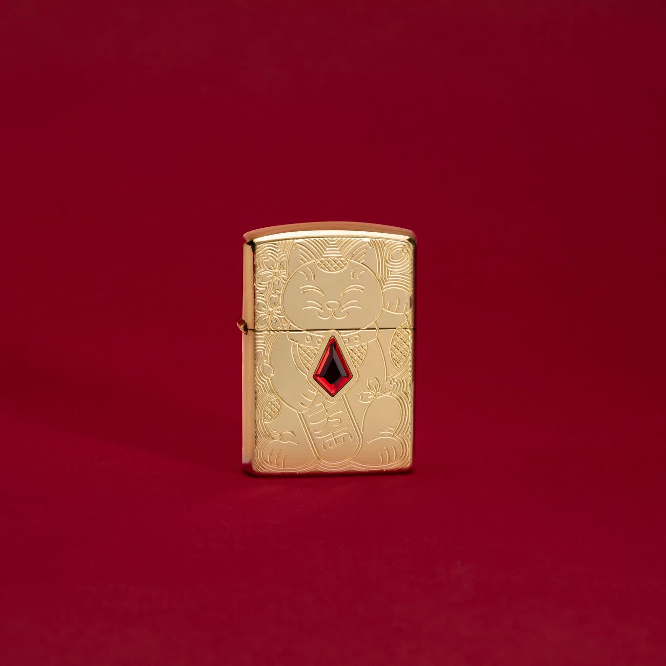 Lifestyle image of Lucky Cat Design Emblem Attached Armor® High Polish Brass Windproof Lighter standing in a red scene.