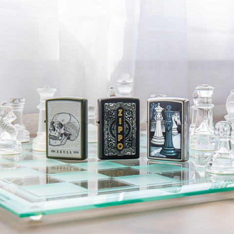 Lifestyle image of Skull Page Design Green Matte Windproof Lighter standing on a glass chess board with a Zippo Themed lighter, a Chess Themed Lighter, and glass chess pieces