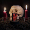 Lifestyle image of Red Skull Design Black Matte Windproof Lighter wit ha skull and lit candles behind it.