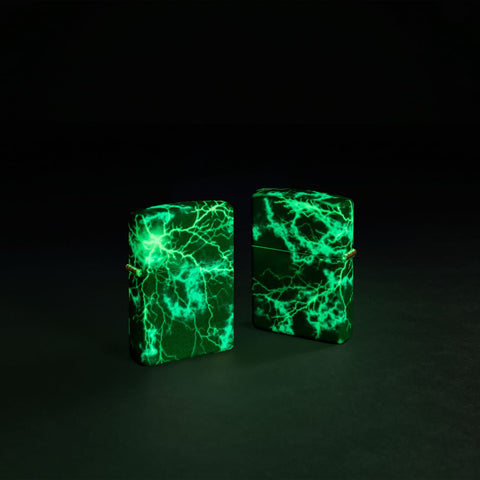 Glamour shot of two Zippo Lightning Design Glow in the Dark 540 Color Windproof Lighters, one showing the front and the other showing the back, glowing in the dark.
