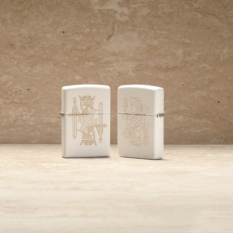 Lifestyle image of two King Queen Design White Matte Windproof Lighters, one showing the front and the other showing the back of the lighter.
