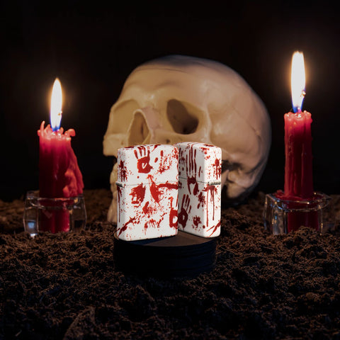 Lifestyle image of two Bloody Hand Design 540 Color Windproof Lighters, one showing the front and the other showing the back with a skull and candles in the background.