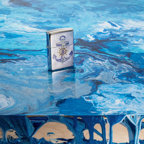 Lifestyle image of Anchor Design High Polish Chrome Windproof Lighter standing on a blue piece of art