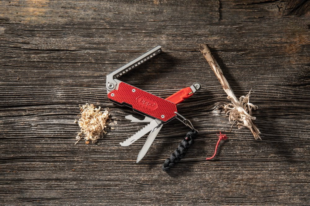 Lifestyle image of Zippo Fire Starting Multi-Tool laying on a wooden surface with tinder shreds and a stick laying next to it.